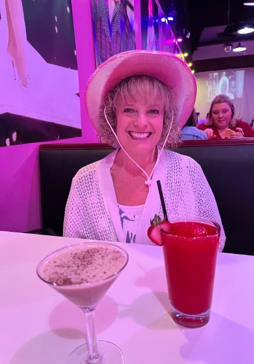 woman with pink cowgirl hat sitting at table with 2 cocktails